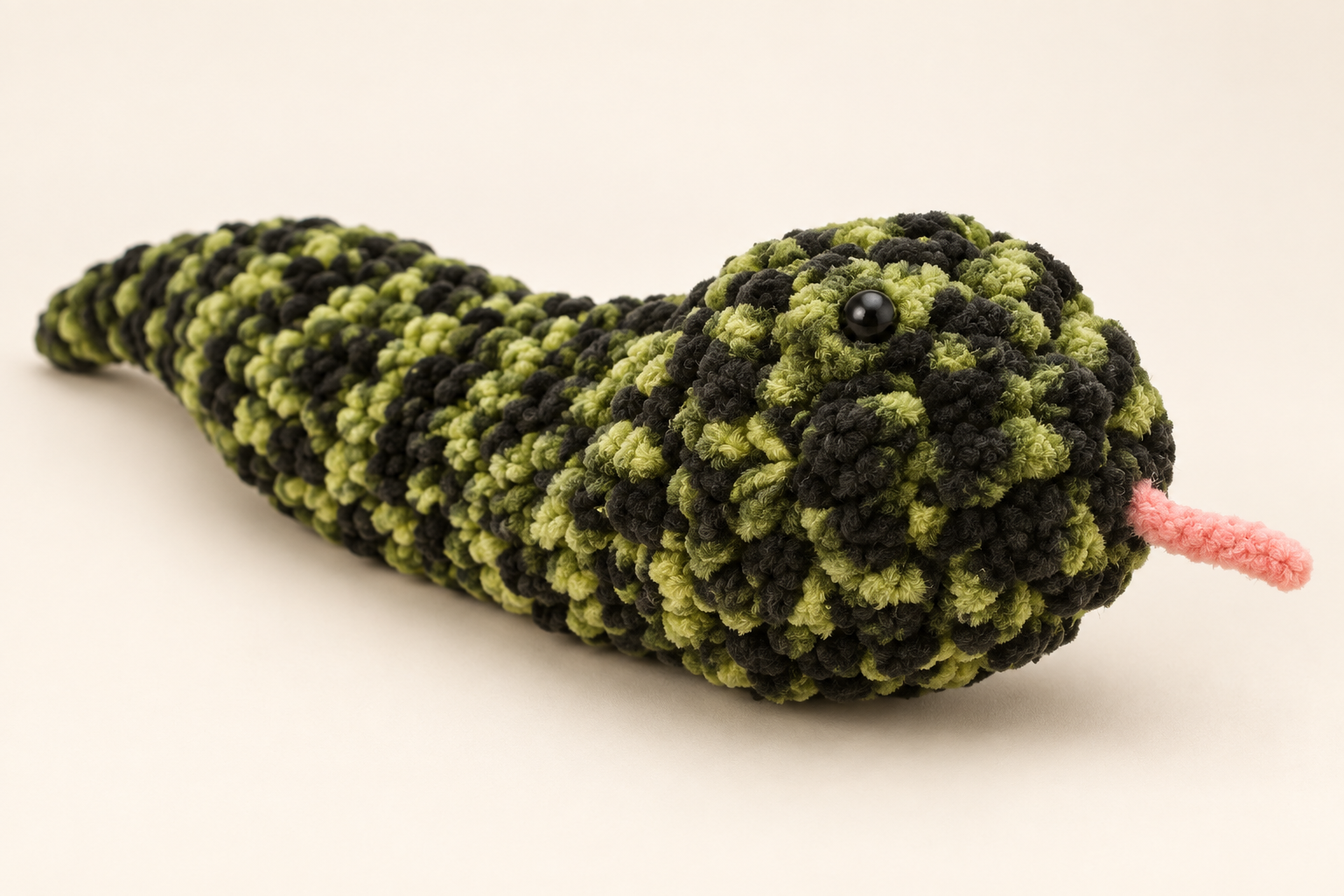 Styled preview of a green and black crochet snake plush with a pink tongue
